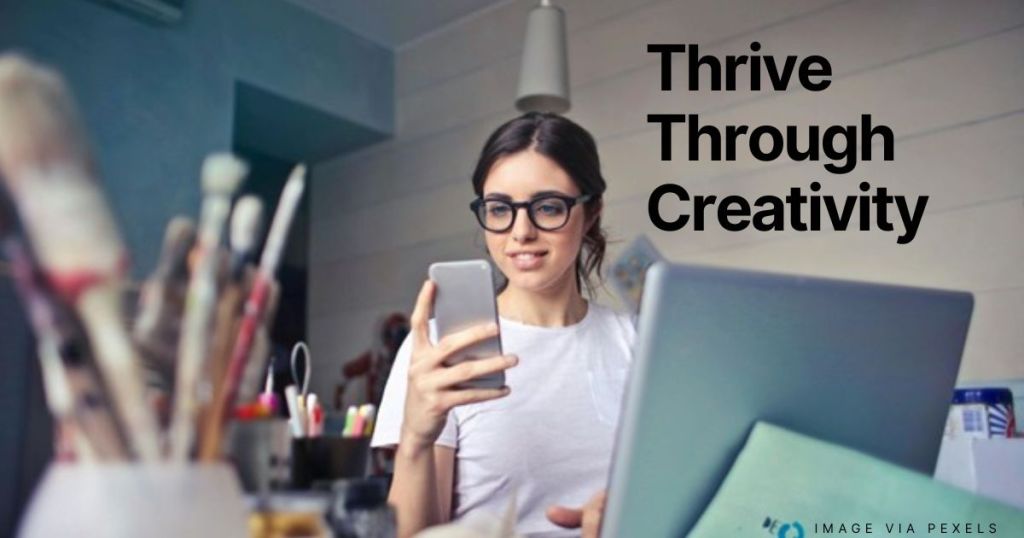 Woman in front of computer smiling with art supplies in the foreground.