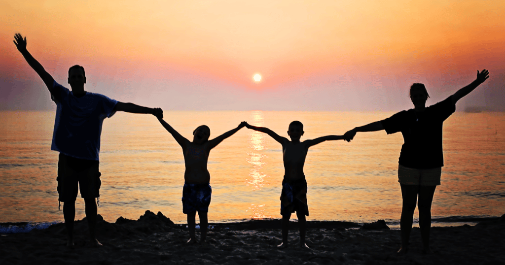 Family all holding hands in front of a sunset over water